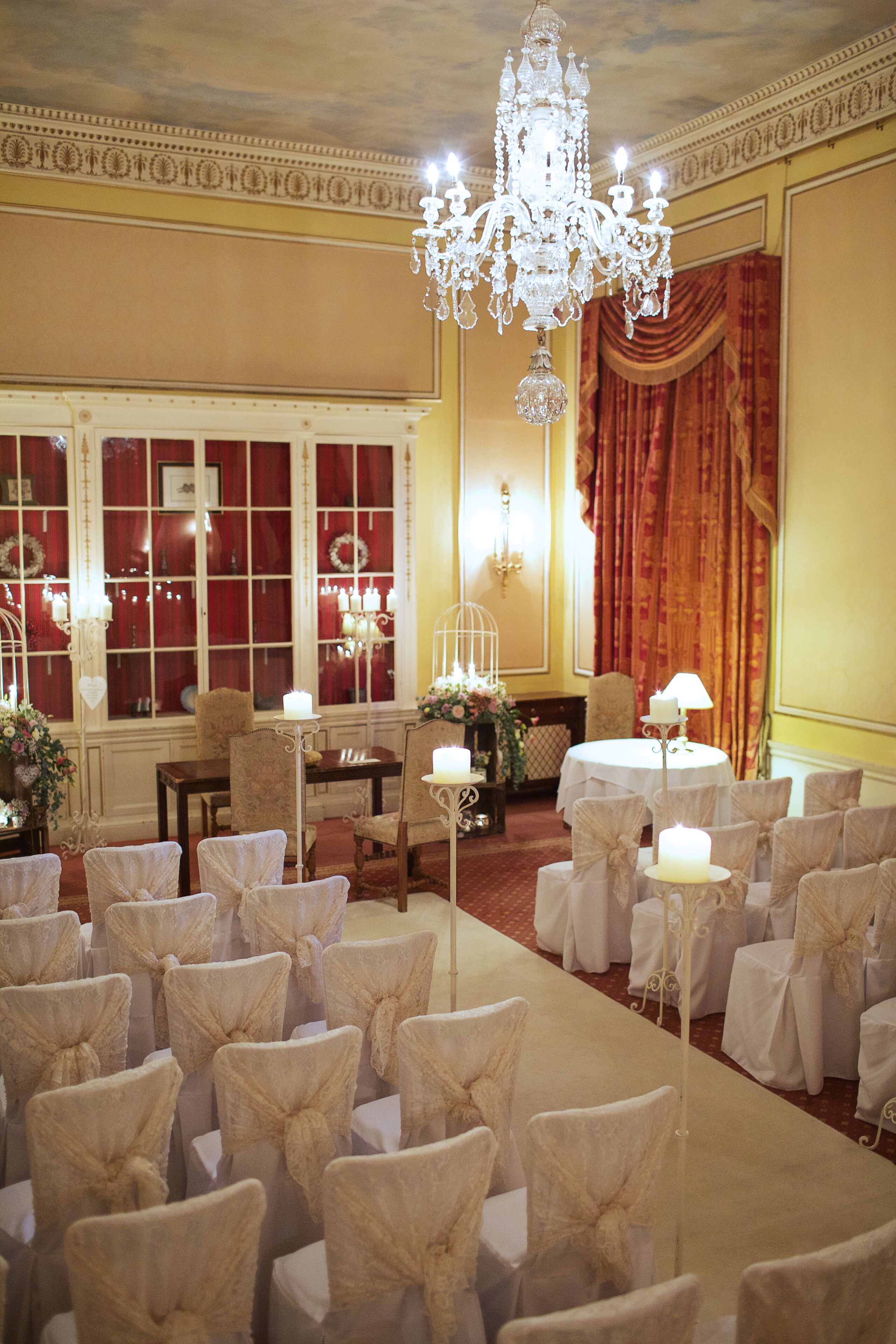 Une salle à l’atmosphère formelle, avec des rangées de chaises, un lustre et une table sur laquelle se trouve une lampe.
