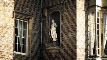 A statue in a niche on a brick building with two windows.