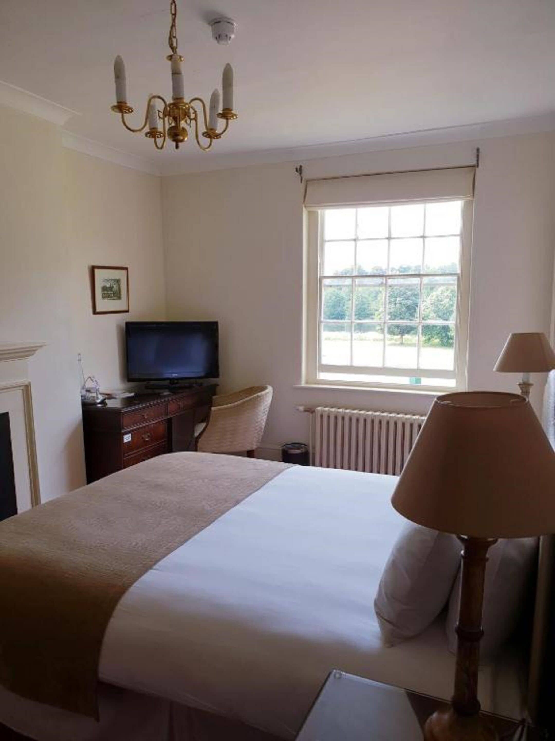 A hotel room with a bed, a television on a dresser, a window with curtains, and a lamp.