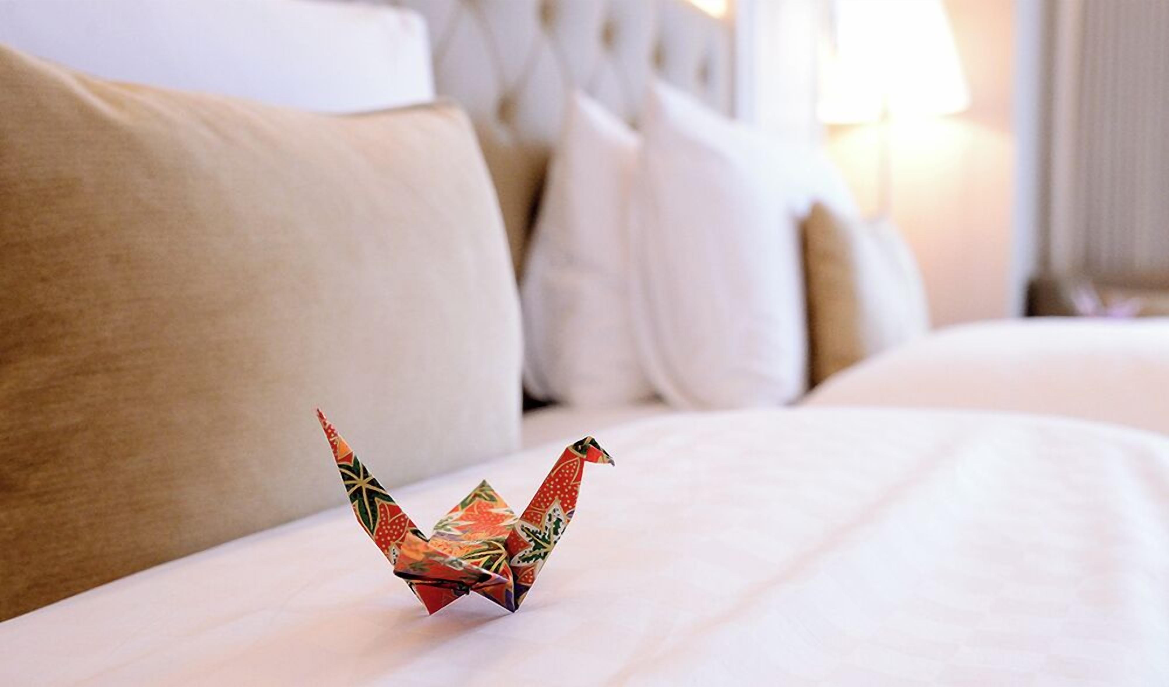 Una cama bien hecha con una grulla de origami decorativa sobre la almohada.