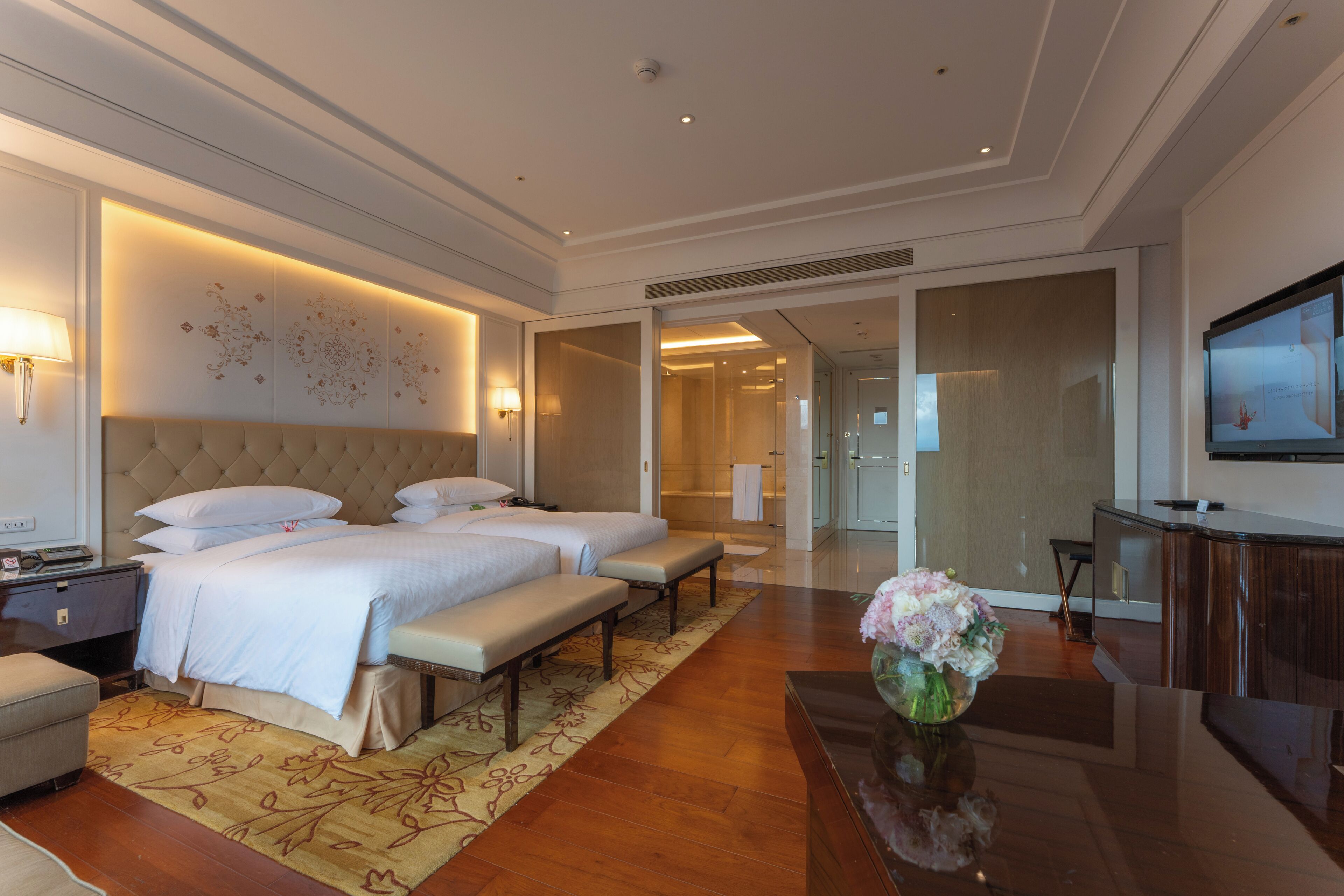 Ein Hotelzimmer mit einem großen Bett, einer Bank, einem Schreibtisch und einem Fernseher.