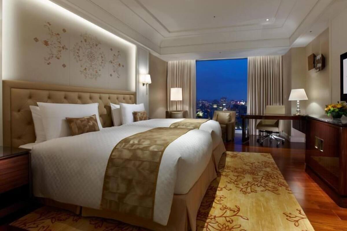 Une chambre d’hôtel avec un grand lit, un bureau et une vue sur la ville la nuit.