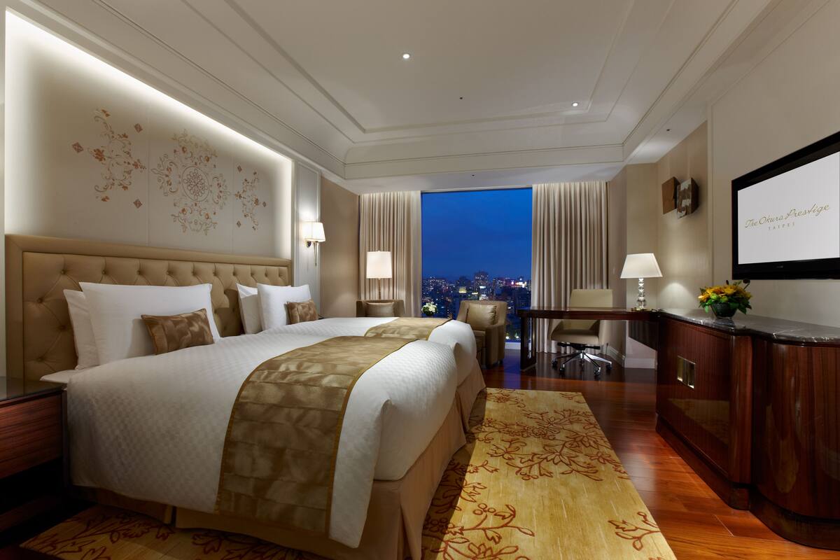 Une chambre d’hôtel avec un grand lit, un bureau et une vue sur la ville la nuit.