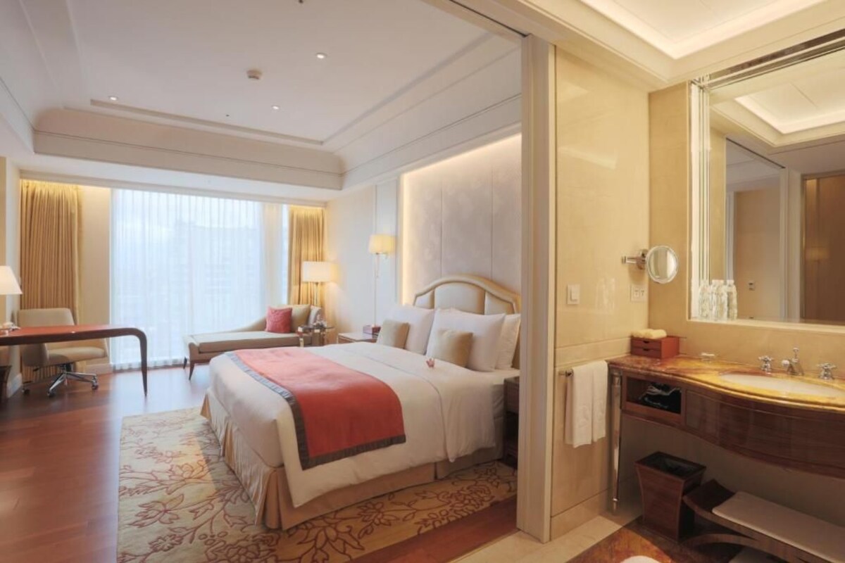 Een hotelkamer met een groot bed, een bureau, een stoel, een kaptafel met spiegel en een badkamer met wastafel en toilet.