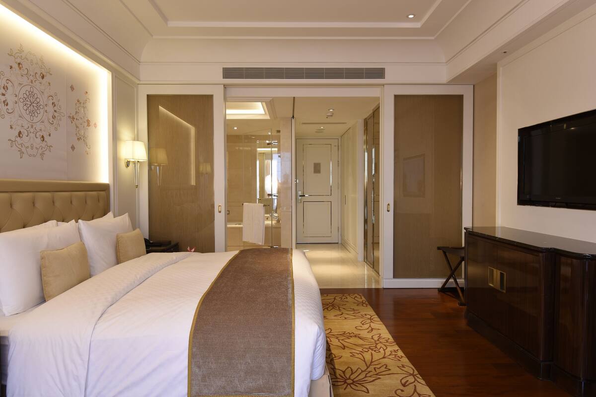 Une chambre d’hôtel avec un grand lit, une télévision, un bureau et une salle de bain visible à travers une porte ouverte.