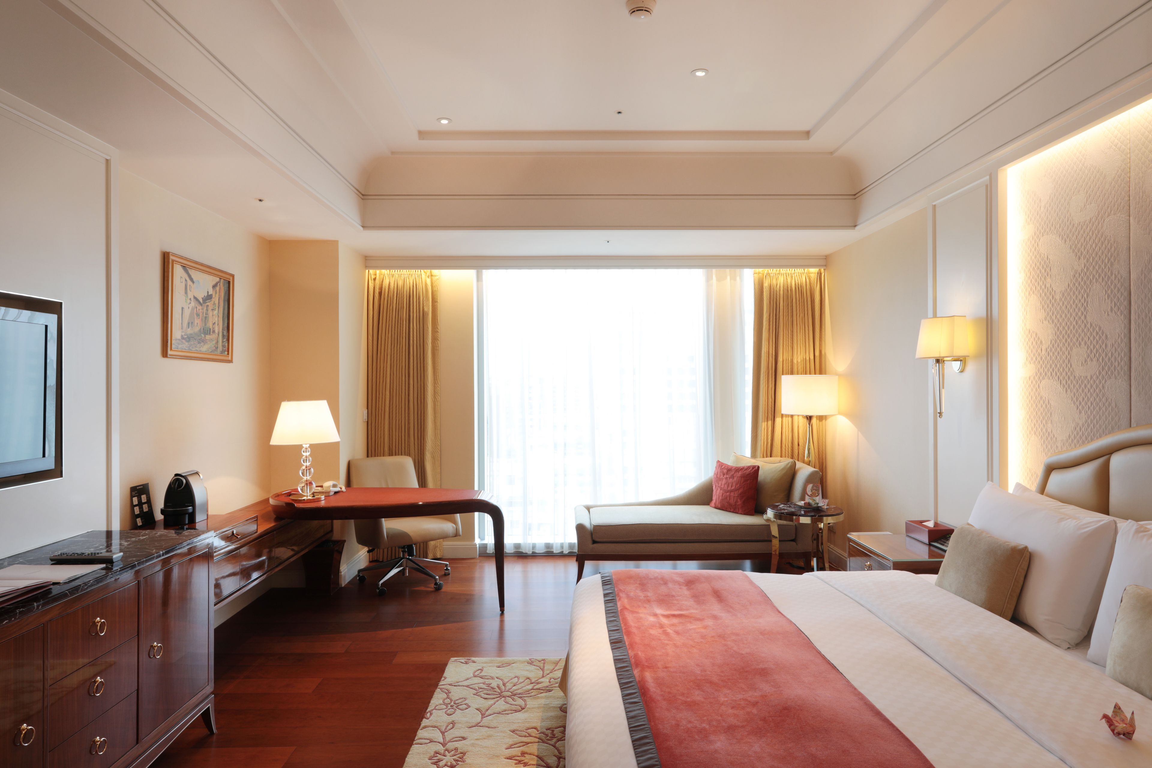 A hotel room with a bed, a desk, a chair, a TV, and a window with curtains.