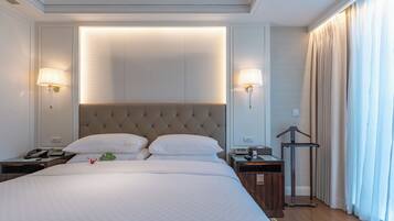 A hotel room with a large bed, two bedside tables, a hanging light fixture, and a window with curtains.
