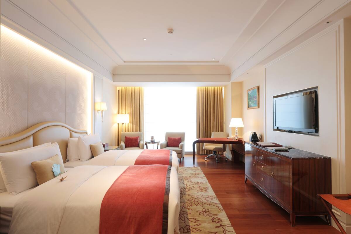Une chambre d’hôtel avec deux lits, un bureau, une télévision et une commode.