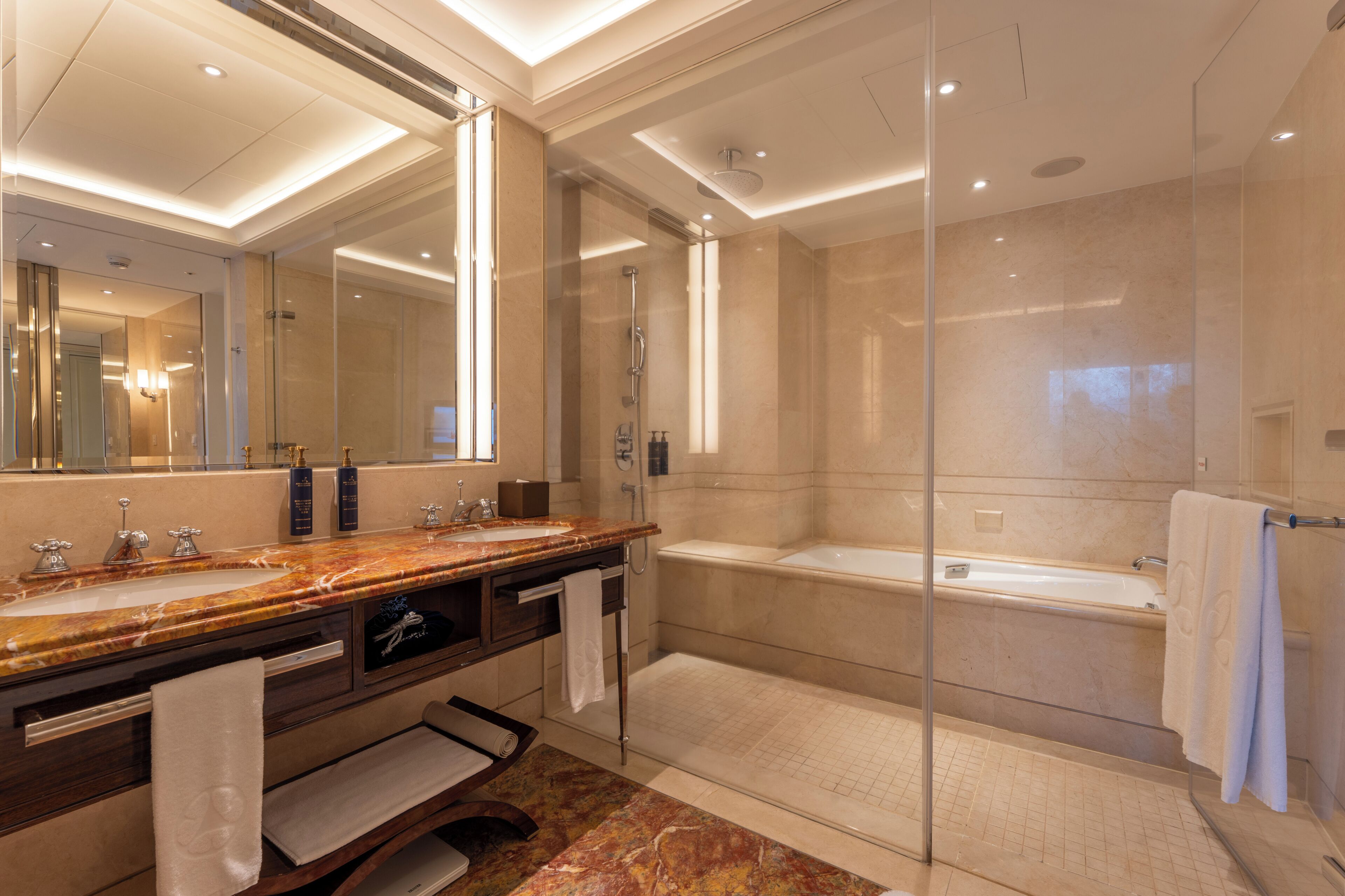 A modern bathroom with a marble vanity, a large mirror, a glass-enclosed shower, and a separate bathtub.