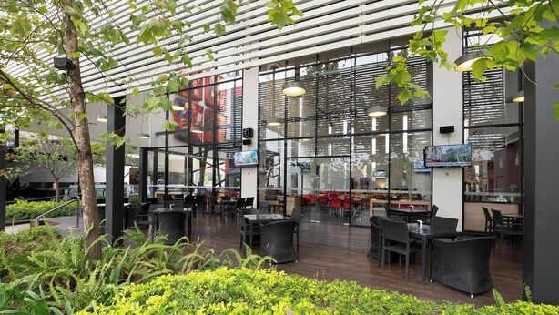 An outdoor dining area with tables and chairs, surrounded by greenery and a modern architectural design with glass walls. - Ramada Encore by Wyndham Guadalajara Sur (Tlajomulco de Zúñiga)