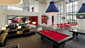 A modern indoor pool area with a red pool table, lounge seating, and large blue pendant lights. - Ramada Encore by Wyndham Guadalajara Sur (Tlajomulco de Zúñiga)