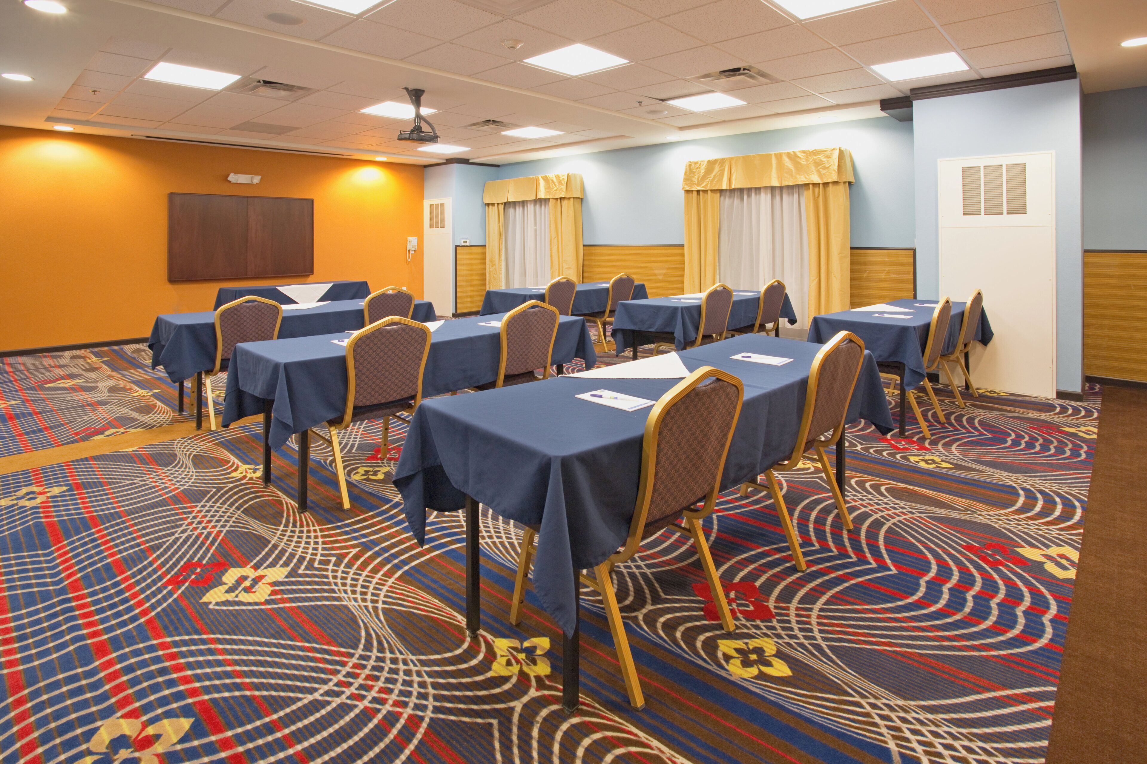 A conference room with multiple tables and chairs, a patterned carpet, and a ceiling with recessed lighting.