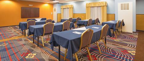 A conference room with multiple tables and chairs, a patterned carpet, and a ceiling with recessed lighting.