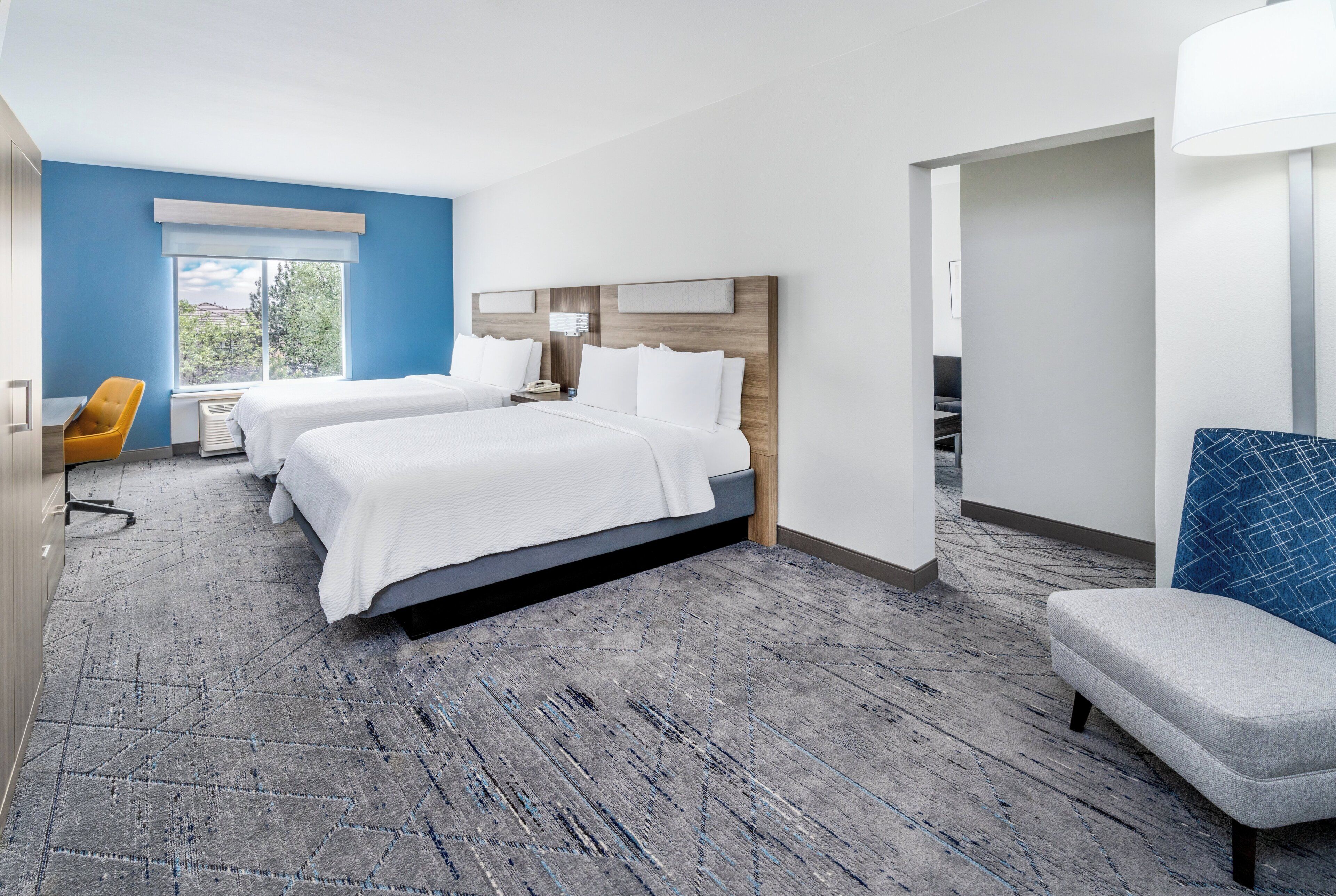 A hotel room with two beds, a desk, a chair, and a large window.