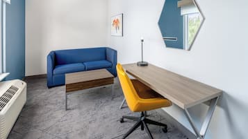 Un espacio de oficina moderno con un sofá azul, un escritorio de madera, una silla amarilla y un espejo hexagonal llamativo.