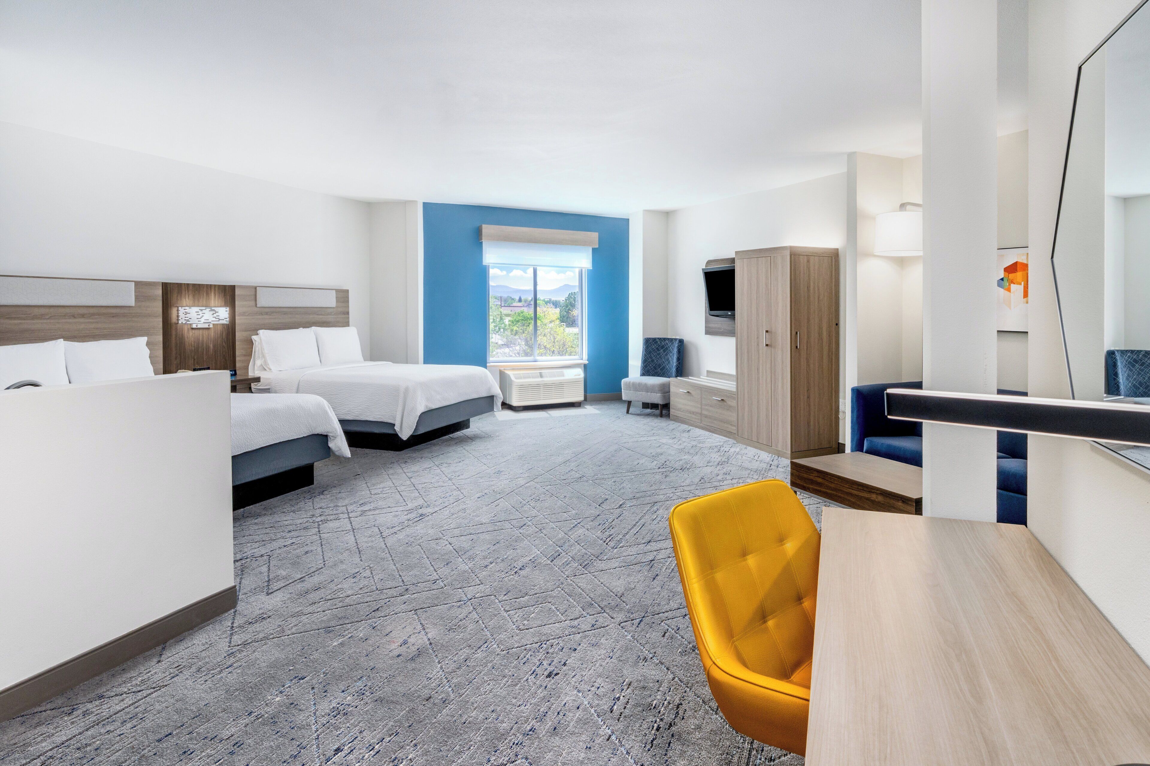 A hotel room with two beds, a desk, a chair, a wardrobe, and a large window offering a view.