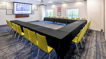 Un salón de conferencias con una larga mesa, sillas amarillas y una pantalla de proyección que muestra el logotipo de Holiday Inn Express.