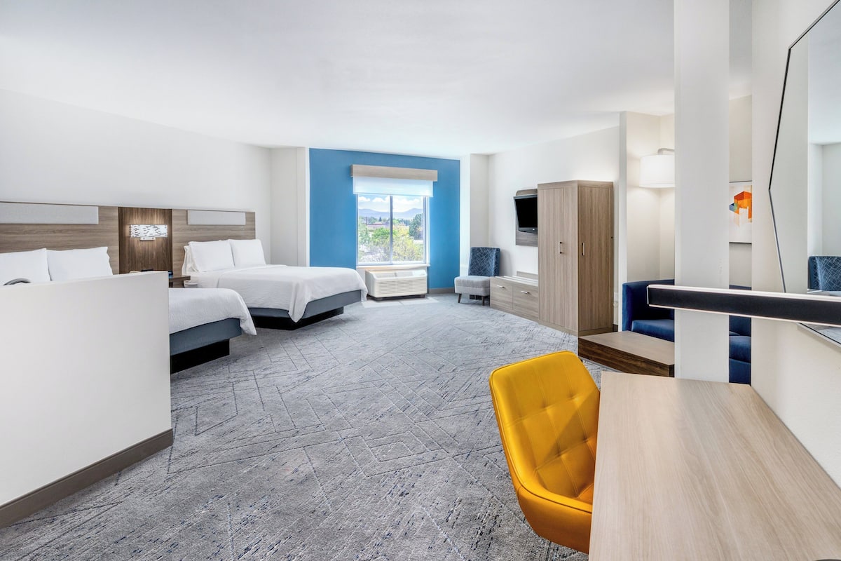 A hotel room with two beds, a desk, a chair, a wardrobe, and a large window offering a view.