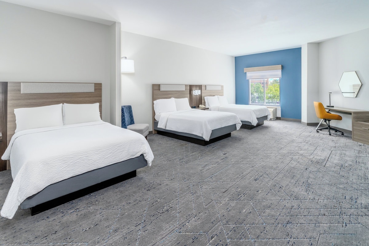 A hotel room with three beds, a desk, and a chair.
