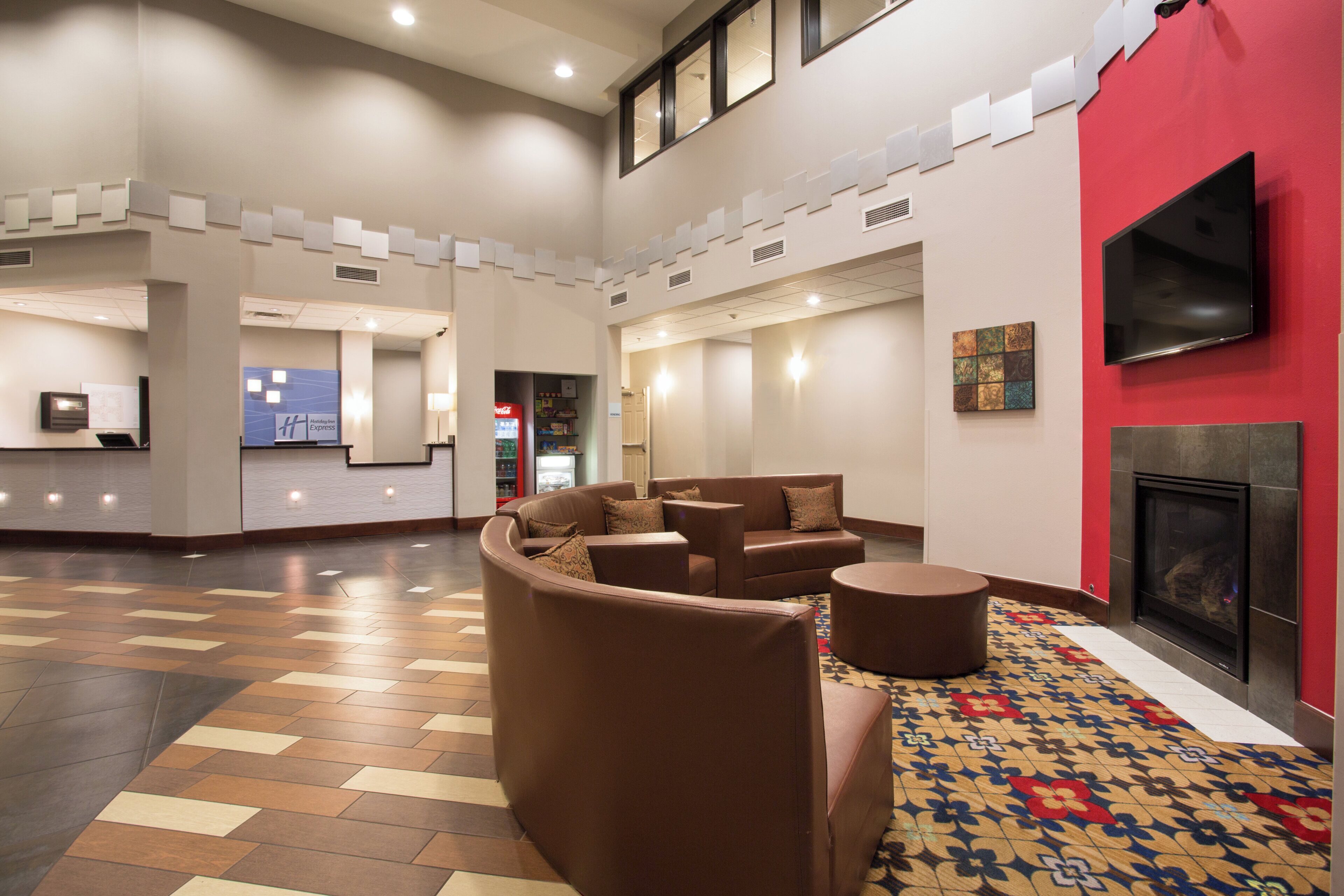 A hotel lobby with a seating area, a fireplace, and a flat-screen TV mounted on the wall.