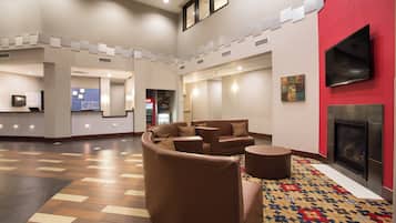 A hotel lobby with a seating area, a fireplace, and a flat-screen TV mounted on the wall.