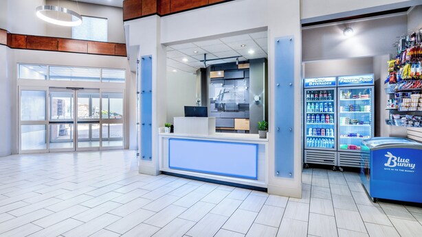 A modern reception area with a counter, a coffee machine, and vending machines. - Holiday Inn Express Hotel & Suites Denver North - Thornton by IHG (Thornton)