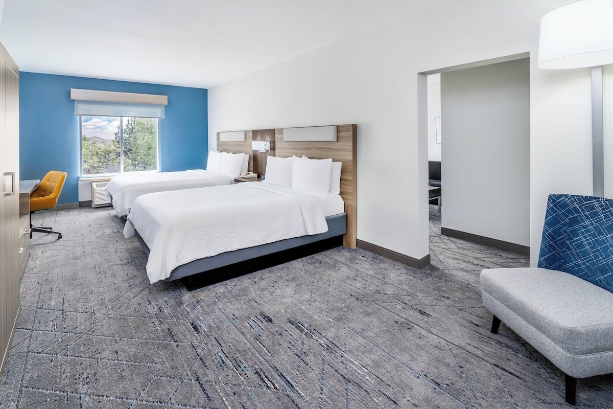 A hotel room with two beds, a desk, a chair, and a large window.