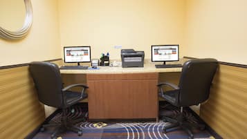 A hotel room with a desk, two monitors, a printer, and two chairs.