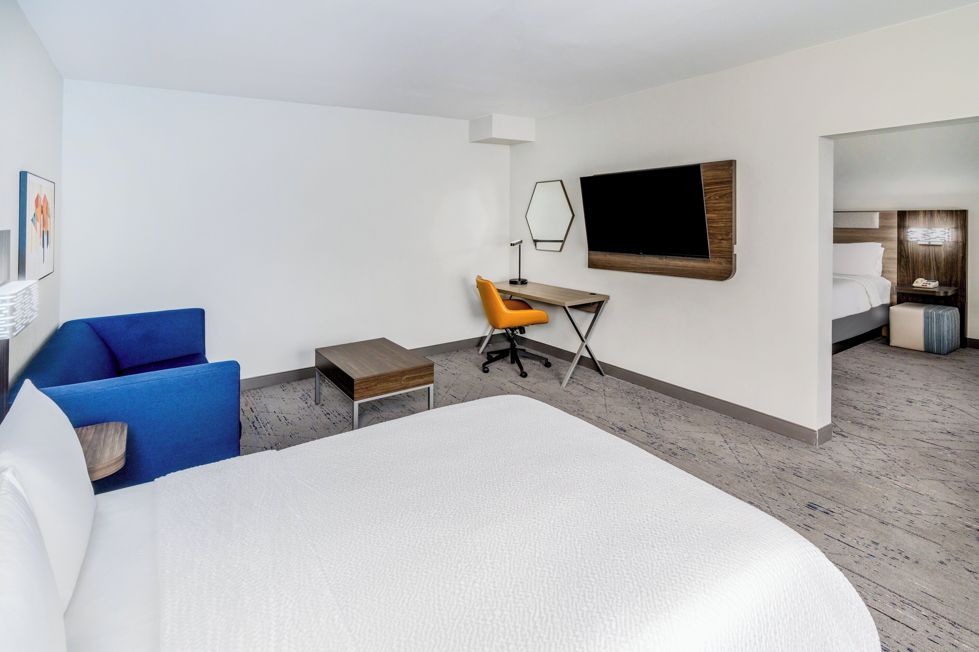 Habitació d'hotel amb un llit gran, una escriptori amb una cadira, un televisor i una zona de dormir separada.