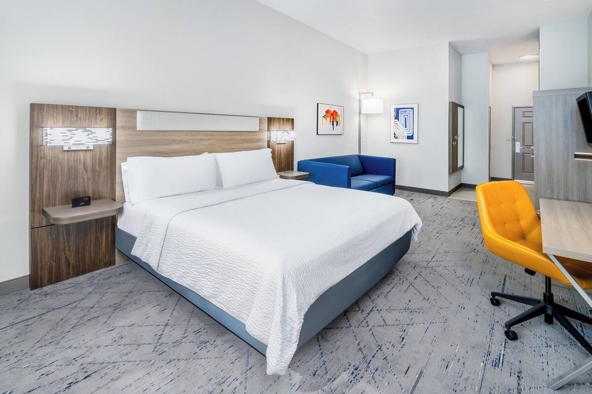 A modern hotel room with a large bed, a desk, a chair, and a sofa.