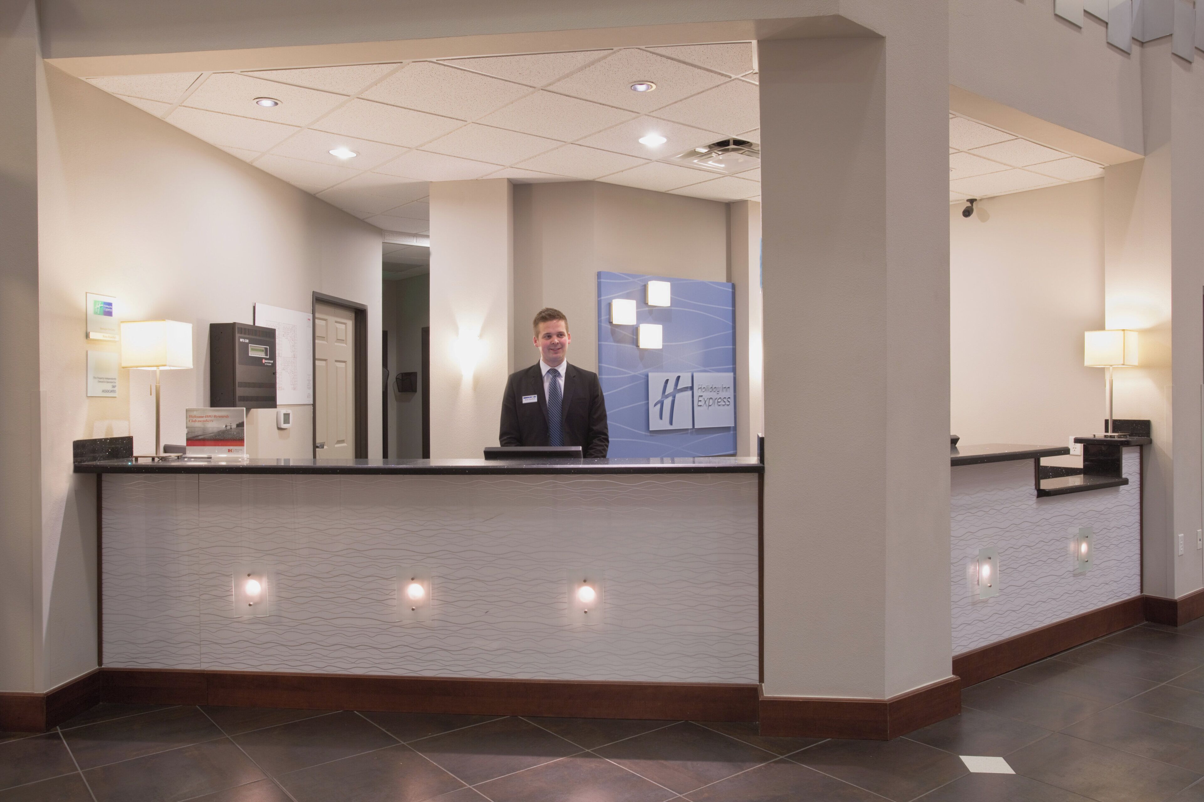 En hotelreception med en navneskilte, en digital skærm og et venteområde.