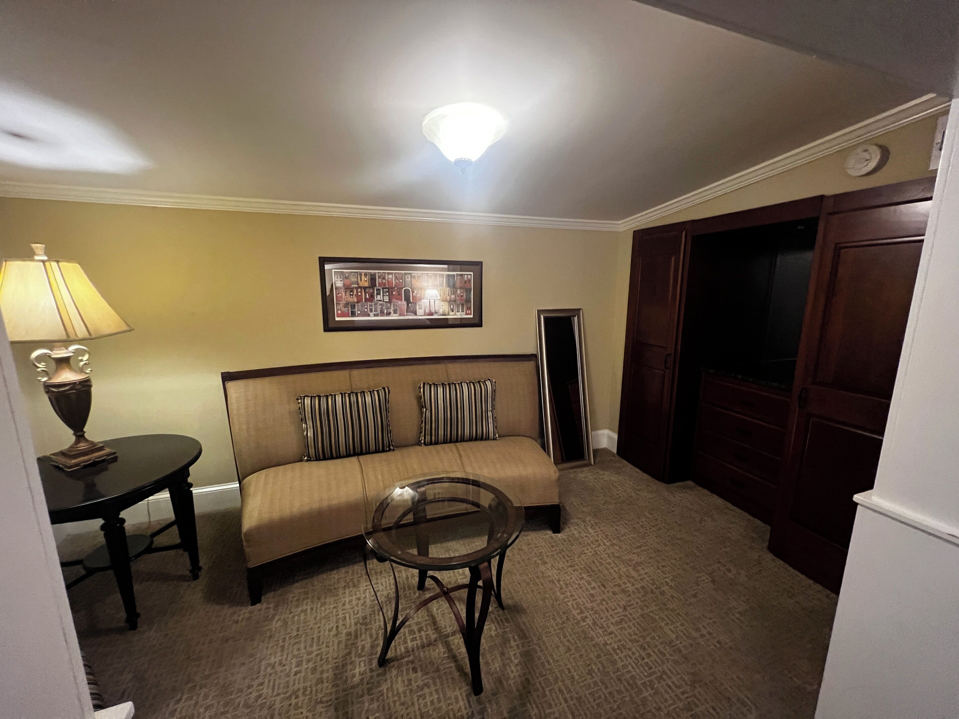 A living room with a sofa, a small round table, a lamp, a framed picture on the wall, and a door.