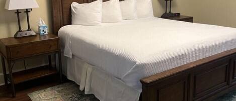 A bedroom with a large bed, two bedside tables, a nightstand, a rug, and a painting on the wall.