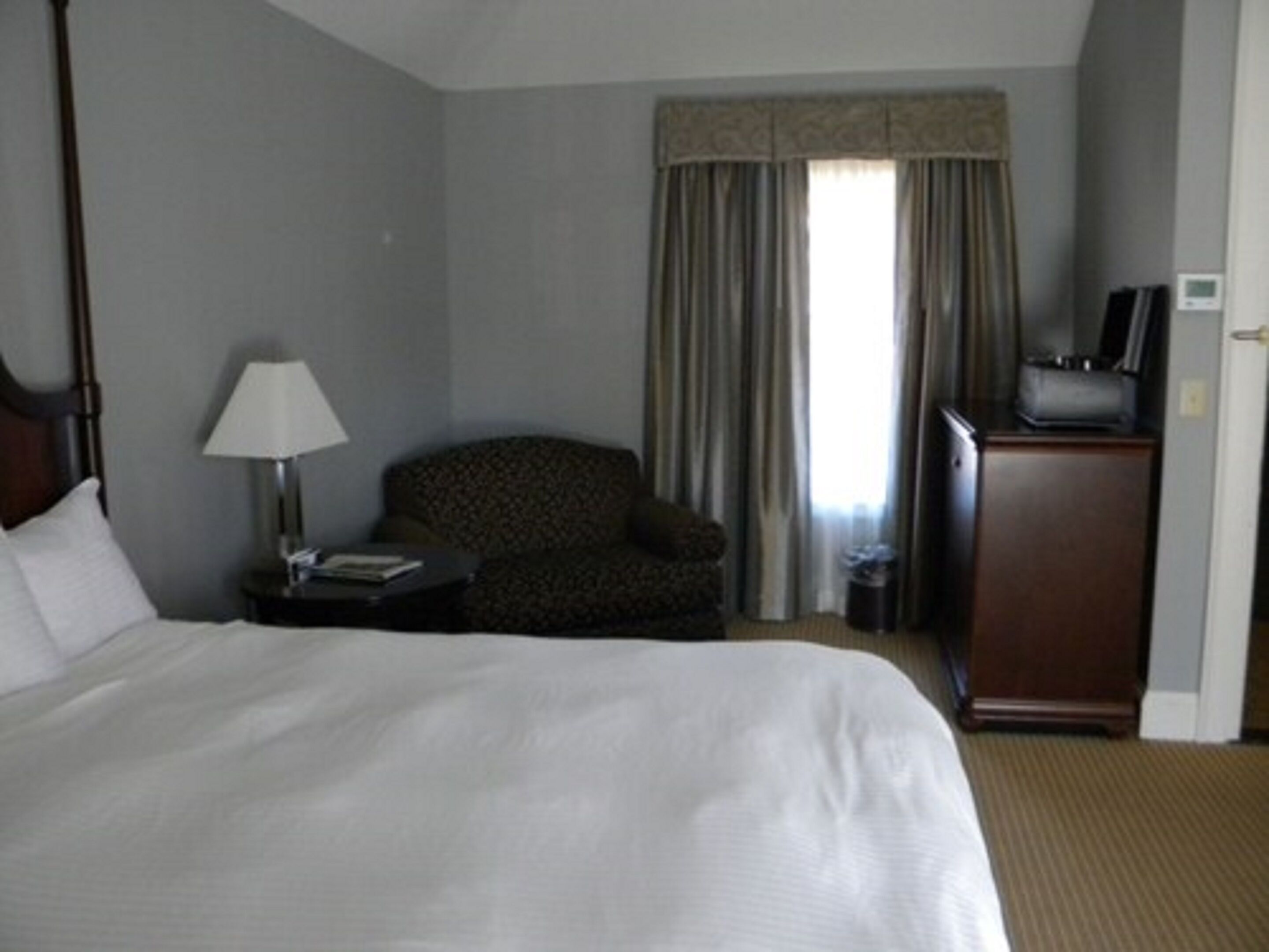 A hotel room with a large bed, a chair, a desk with a lamp, and a television.