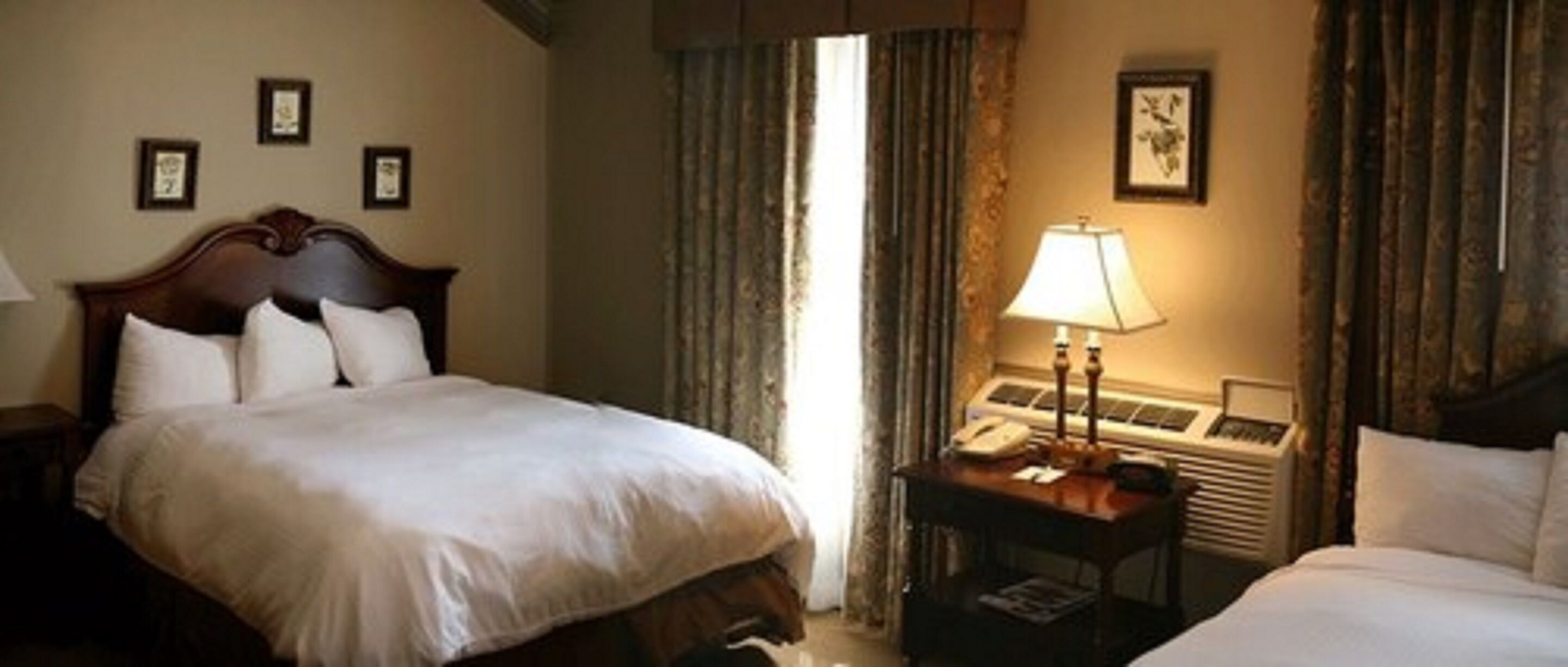 Una habitación de hotel con una cama grande, una mesita de noche con lámpara y una ventana con cortinas.