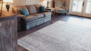 Un salon avec un mur lambrissé en bois, un canapé, un fauteuil à motifs, une lampe et un tableau représentant un arbre.