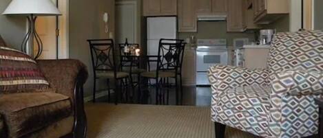 Un salon comprenant un canapé, un fauteuil à motifs, une table à manger avec des chaises, et un coin cuisine avec des placards et des appareils électroménagers.
