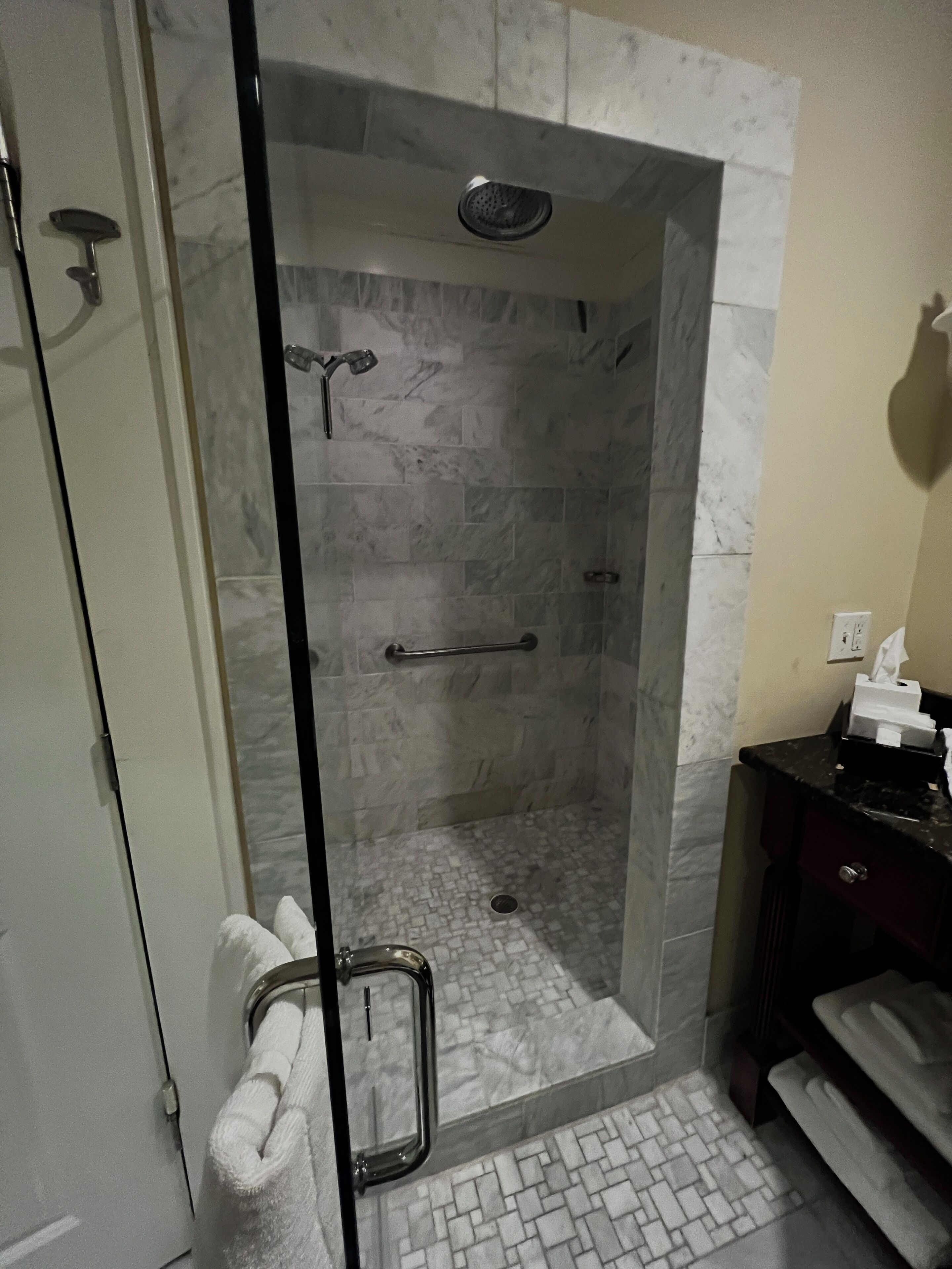 Eine gläserne Dusche mit Marmorboden und Handtuchhalter.