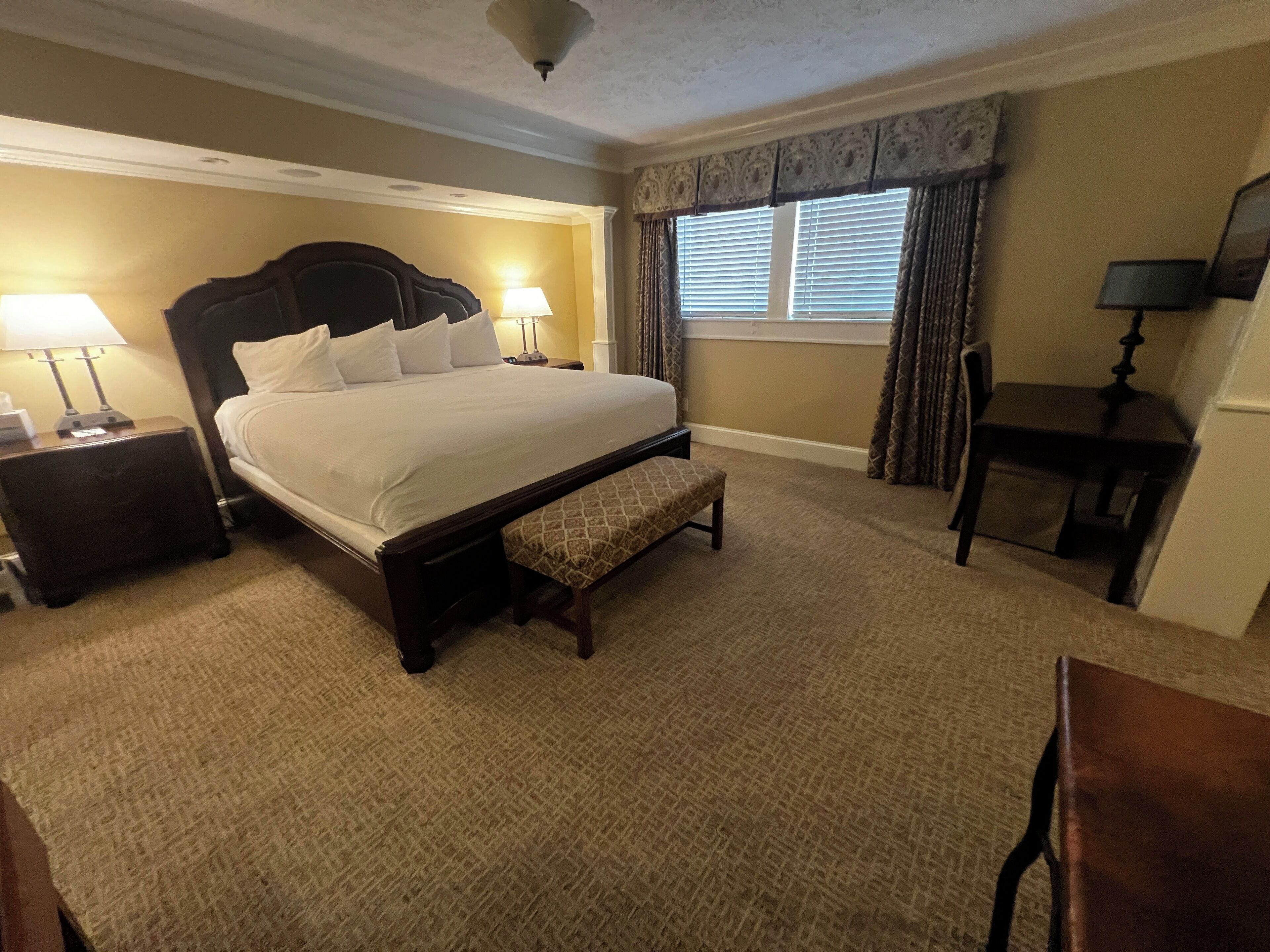 A hotel room with a large bed, bedside tables with lamps, a desk, and a chair.