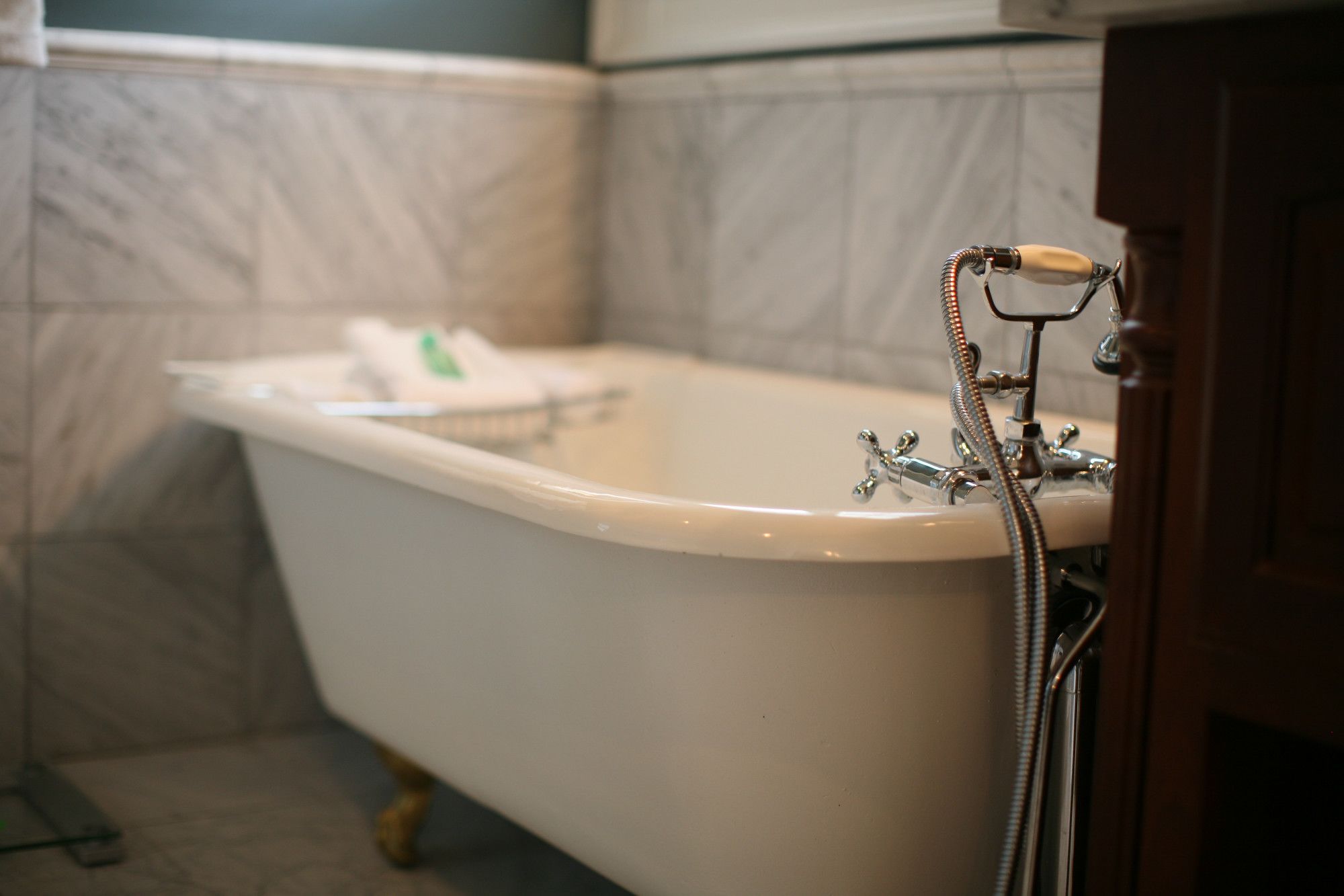 Una bañera tipo pata de león con un cabezal de ducha manual, una toalla y una botella de champú al fondo.