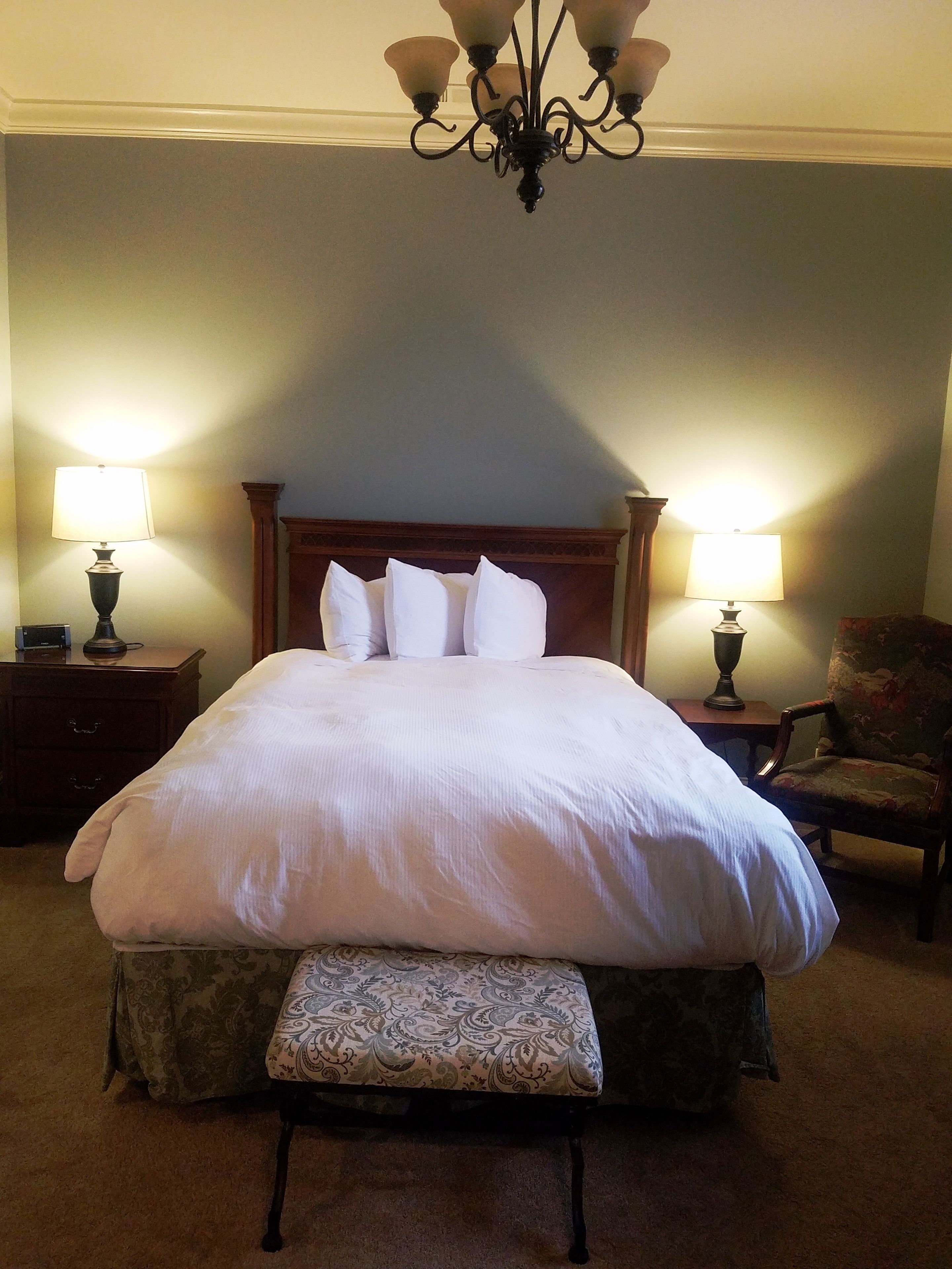 A large bed with a wooden headboard, two bedside lamps, a chair, and a bench.