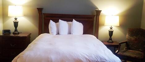 A large bed with a wooden headboard, two bedside lamps, a chair, and a bench.
