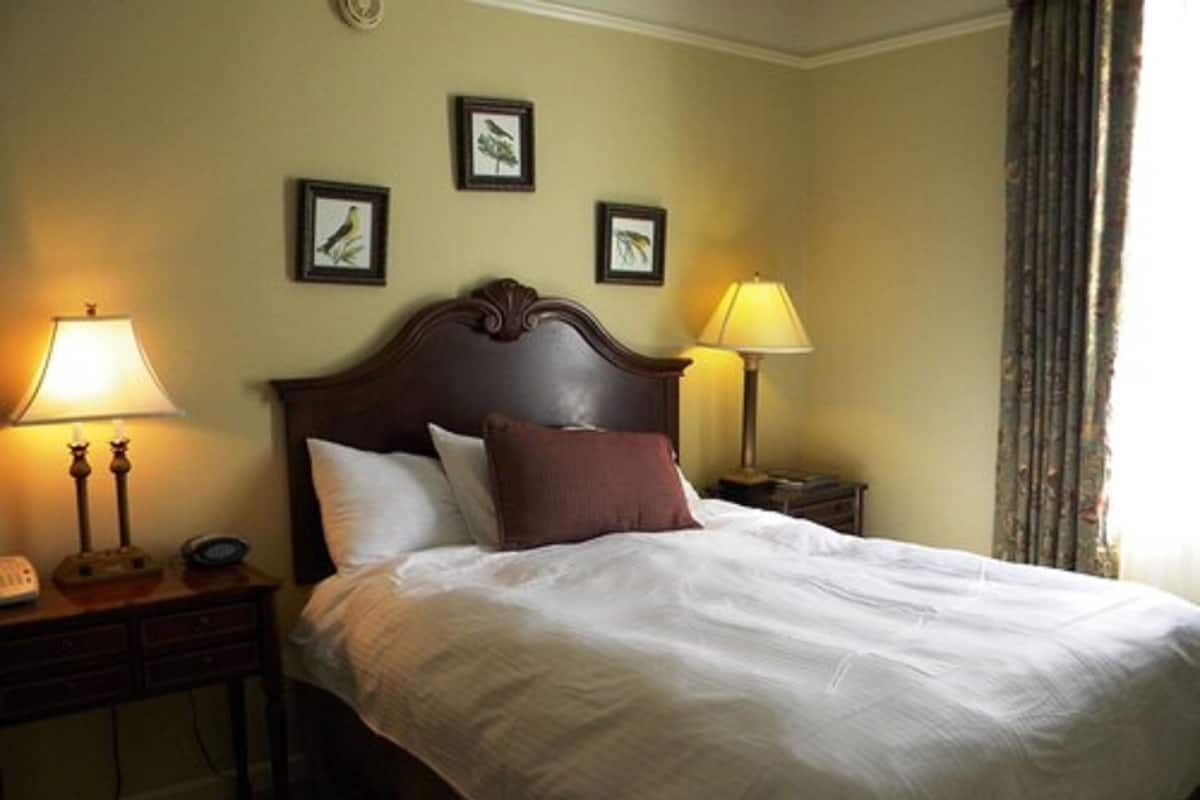 Quarto de hotel com uma cama grande, duas mesas de cabeceira e luminárias fixadas na parede.