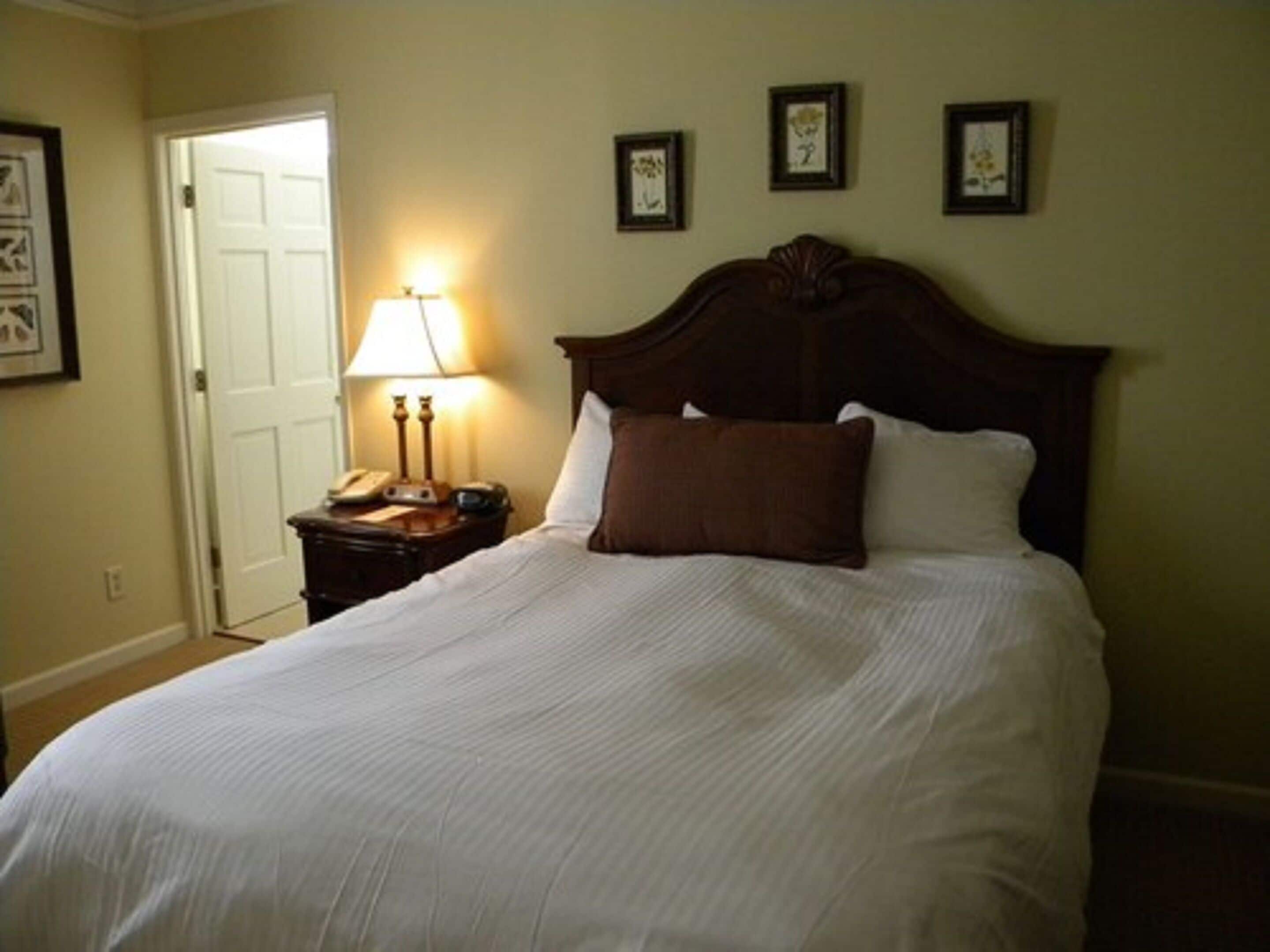 A neatly made bed with a wooden headboard, a bedside lamp, and a nightstand with a telephone.