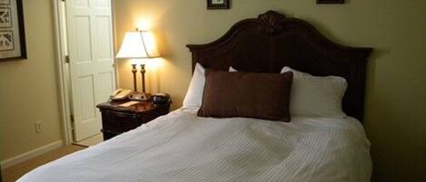 A neatly made bed with a wooden headboard, a bedside lamp, and a nightstand with a telephone.
