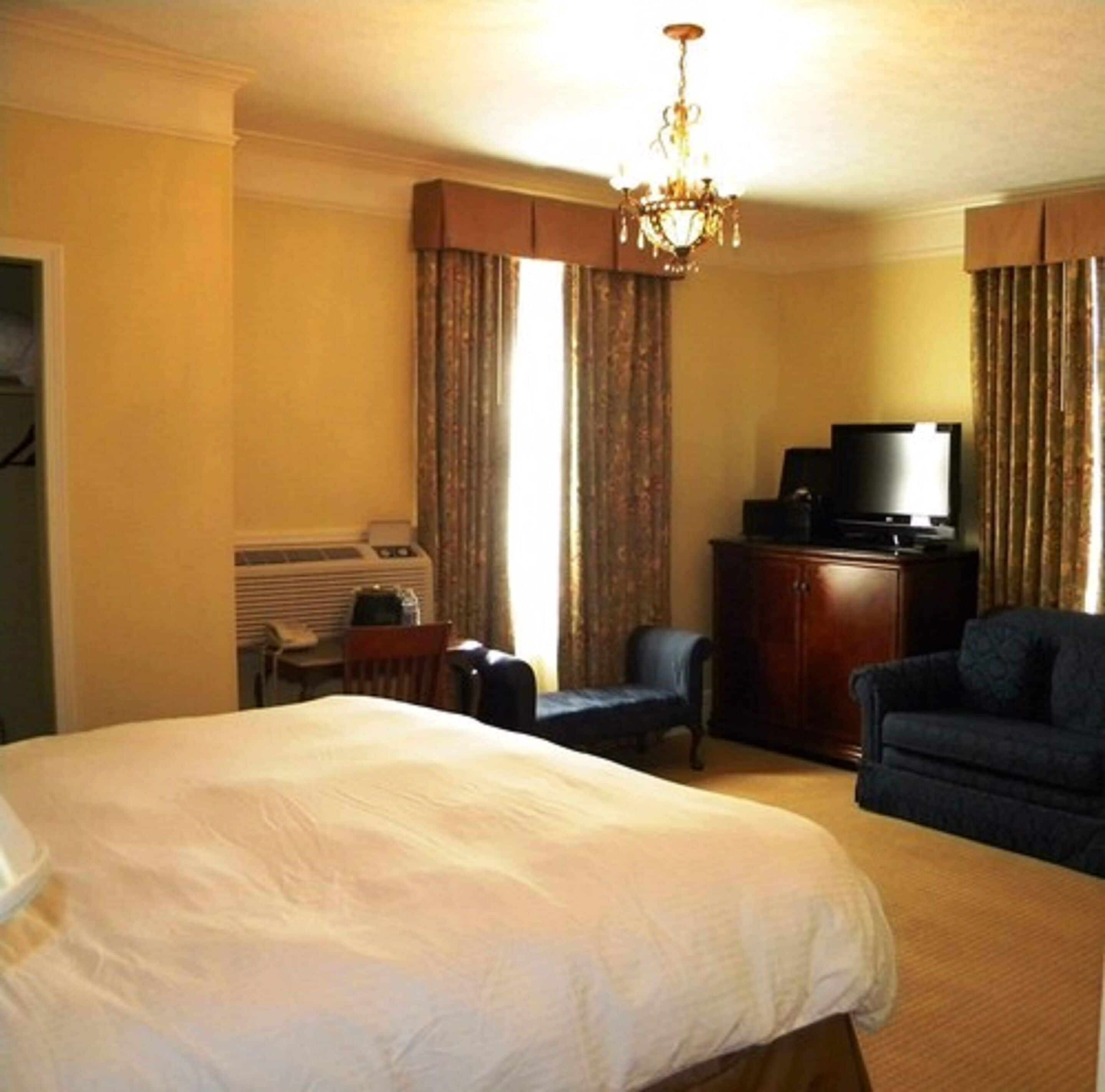 A hotel room with a large bed, a television, a desk with a chair, and a wardrobe.