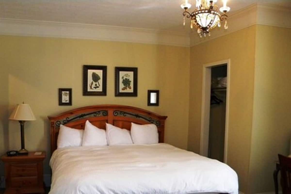 Um quarto com cama, mesa de cabeceira, abajur e lustre.