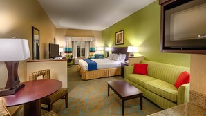 Une chambre d’hôtel avec un lit, un canapé vert, une table à manger avec des chaises, un téléviseur et un bureau avec une lampe.