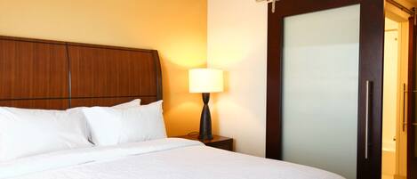 Quarto de hotel com uma cama, mesa de cabeceira, abajur e porta de correr.