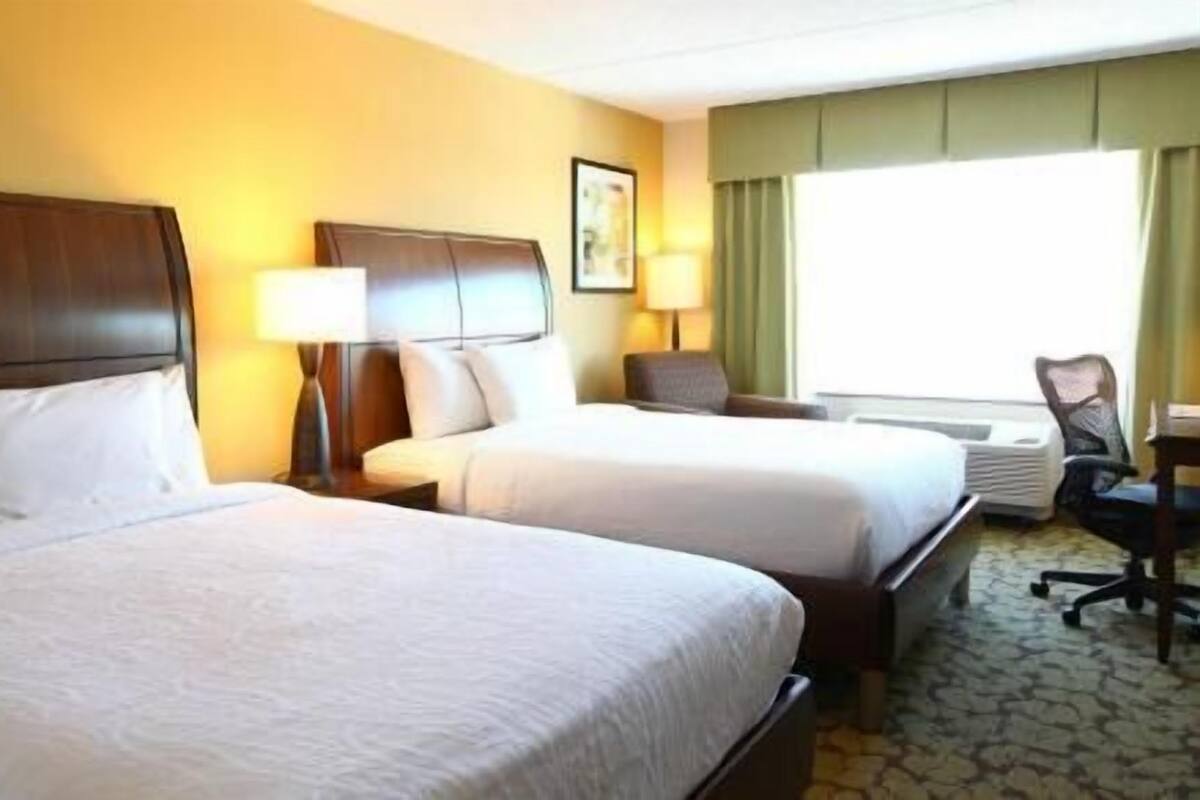 A hotel room with two beds, a desk, a chair, and a window with curtains.